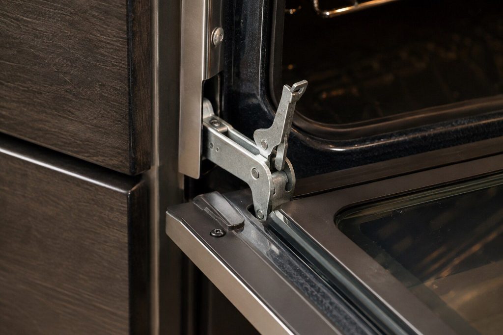 A close view of a hinge arm where it enters the frame of a fully open oven door, with the small locking lever flipped up.