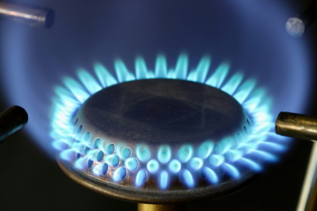 An even ring of blue gas flame around a burner cap, seen close in a dark kitchen