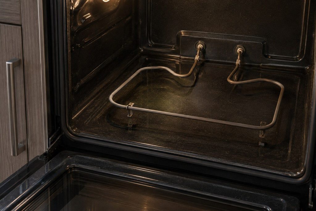 The bottom of an empty oven cavity with the bake element unclipped and lifted a few inches, its two terminals visible where it passes through the back wall.