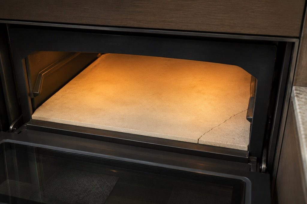 The pale stone floor of a built-in hearth oven seen through the open door, empty, with a fine crack running across one corner of the stone.